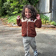 Art Iv is registered to the contest to win money with this photo: bear_patch, casual_clothing, child, curly_hair, daylight, fence, greenery, happy, jacket, nature, outdoor, pants, person, playful, portrait, sidewalk, smiling, sneakers, tree, walking