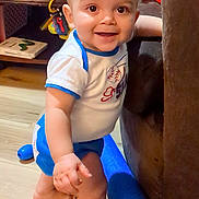 Colter is registered to the contest to win money with this photo: toddler, child, baby, smiling, standing, indoor, living_room, toys, couch, wooden_floor, clothing, shorts, shirt, happy, playtime, furniture, young_child, cute, person, home