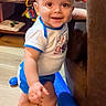 toddler, child, baby, smiling, standing, indoor, living_room, toys, couch, wooden_floor, clothing, shorts, shirt, happy, playtime, furniture, young_child, cute, person, home