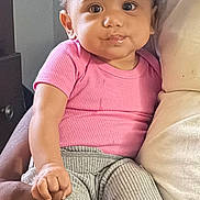 Eliana is registered to the contest to win money with this photo: baby, child, infant, person, pink_shirt, gray_pants, curly_hair, barefoot, hand_holding, smile, indoors, seated, cute, skin, portrait, young, human, cozy, comfort, expression