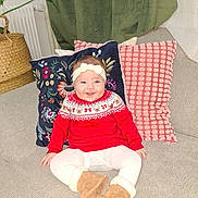 Nourhène a rejoint le concours — aidez-le/la à gagner de superbes lots ! baby, child, smiling, red_sweater, boots, headband, couch, pillow, decor, indoor, plant, radiator, blanket, happy, person, portrait, seated, cozy, festive, home