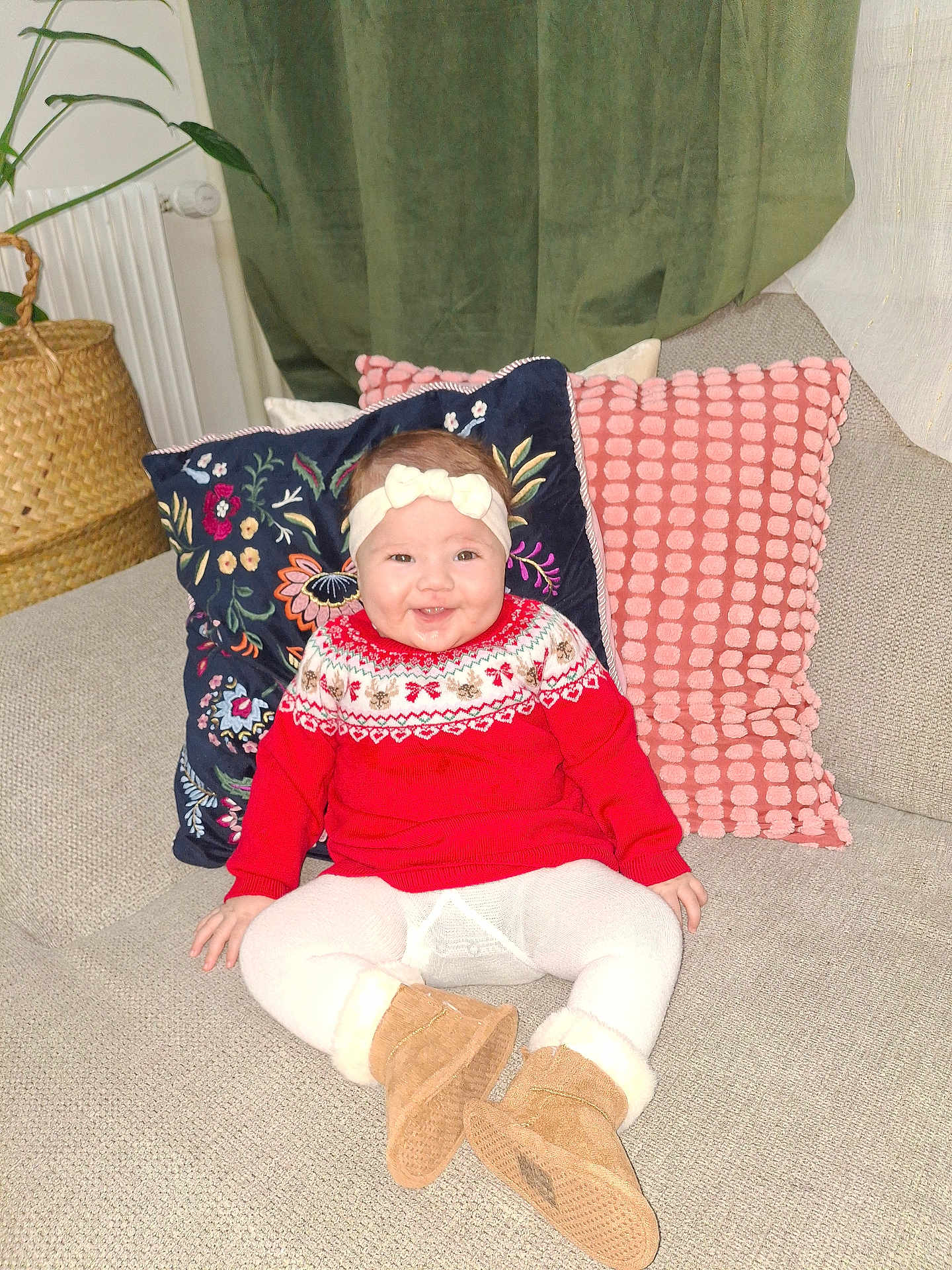 Nourhène a rejoint le concours — aidez-le/la à gagner de superbes lots ! baby, child, smiling, red_sweater, boots, headband, couch, pillow, decor, indoor, plant, radiator, blanket, happy, person, portrait, seated, cozy, festive, home