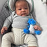 baby, infant, plush_toy, blue_dragon, cushioned_seat, gray_clothing, cream_pants, baby_toys, indoors, child, person, cute, young_child, portrait, seated, comfort, soft_fabric, infant_clothing, hand, face
