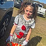 child, clown_costume, face_paint, red_nose, pigtails, halloween_bag, gloves, dress, outdoor, grass, parking_lot, cars, autumn, shadow, sunlight, makeup, smile, portrait, trick_or_treat, playful