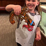 Naevah is registered to the contest to win money with this photo: child, girl, lobster, claws, blue_band, apron, smile, holding, indoor, restaurant, aquarium_tank, wood_paneling, carpet, leggings, shoes, hand, portrait, seafood, happy, earring