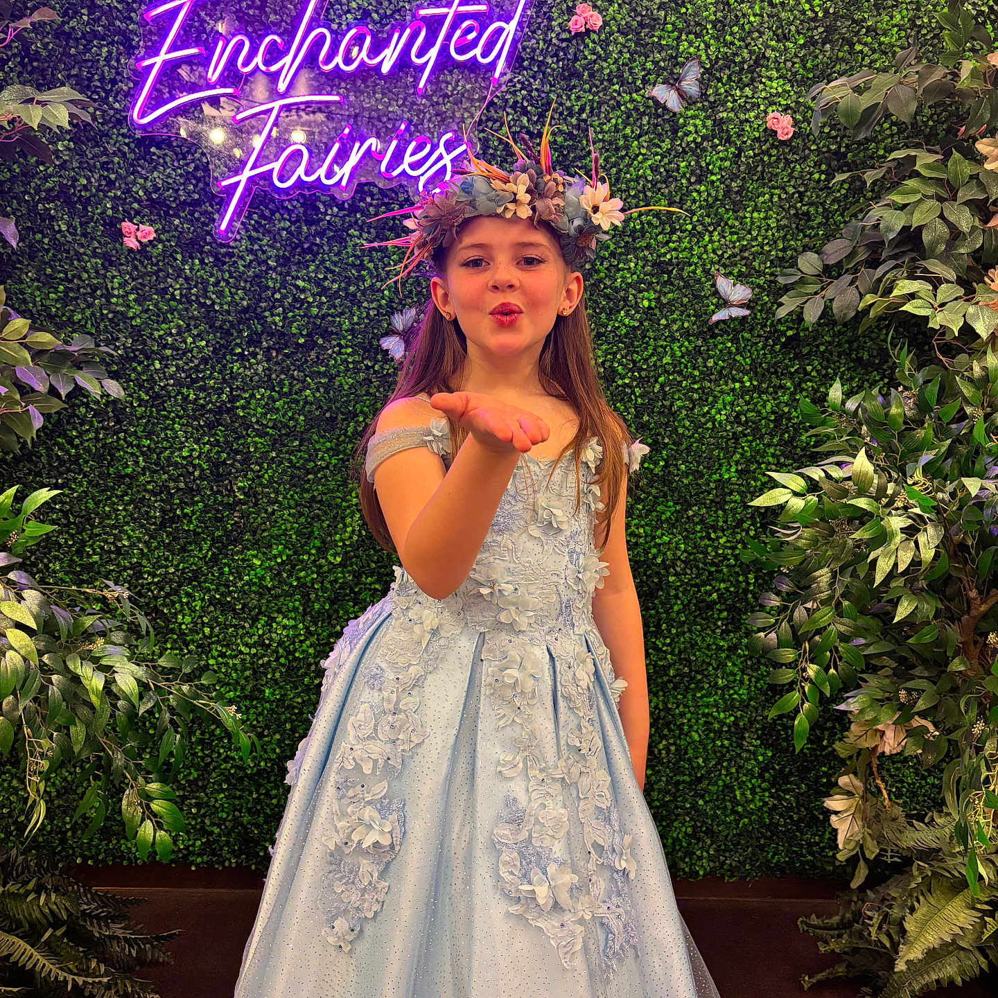 Naevah joined the competition — help win amazing prizes! blowing_kiss, butterflies, child, costume, decor, dress, event, fairy_theme, floral_headpiece, flower_crown, girl, gown, green_wall, indoor, long_hair, neon_sign, photography, portrait, pose, smile