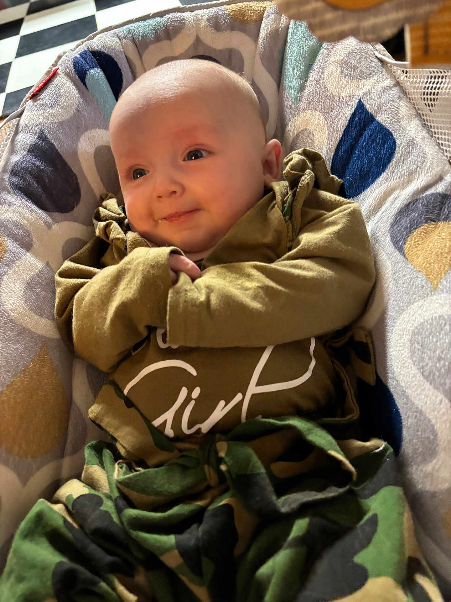 Nayeli is registered to the contest to win money with this photo: baby, infant, newborn, smile, face, head, eyes, hands, cozy, bouncer, blanket, patterned_blanket, camo_print, clothing, onesie, portrait, indoor, soft_lighting, adorable, relaxed