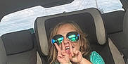 Ophelia-Rayne joined the competition — help win amazing prizes! child, car_seat, sunglasses, peace_sign, car_interior, seatbelt, wristbands, turquoise_shirt, smiling, happy, young_child, reflection, casual_clothing, sitting, vehicle, backseat, playful, blond_hair, daylight, portrait