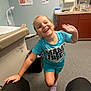 Ophelia-Rayne is registered to the contest to win money with this photo: child, smiling, blue_clothing, medical_office, poster, cabinet, floor, carpet, person, waving, shorts, shoes, earrings, desk, trash_can, countertop, light, happy, indoor, playful