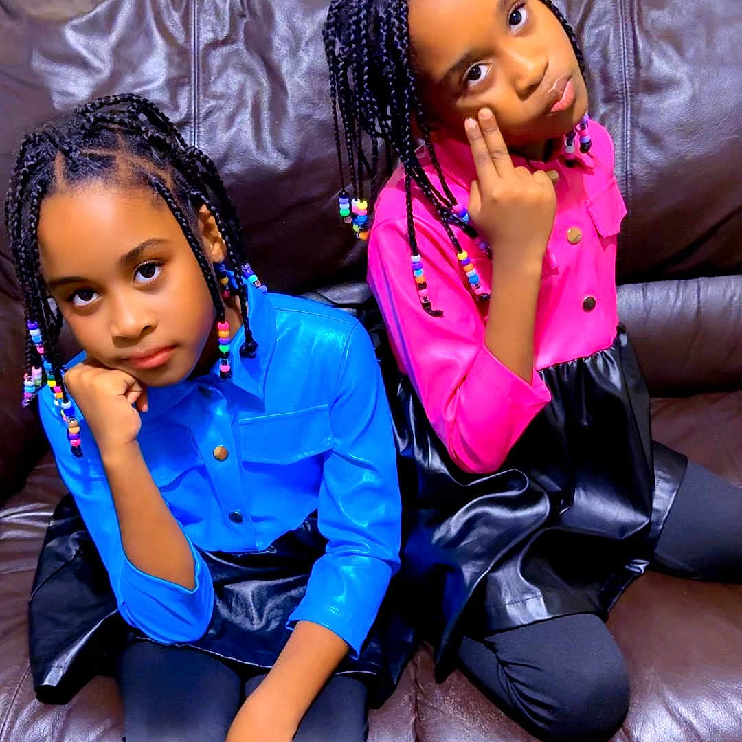 Arianna And Brianna is registered to the contest to win money with this photo: beads, black_skirt, blue_shirt, braided_hair, brown_couch, child, colorful, cute, expression, fashion, furniture, girl, hair_accessories, indoor, leggings, person, pink_shirt, portrait, pose, sitting