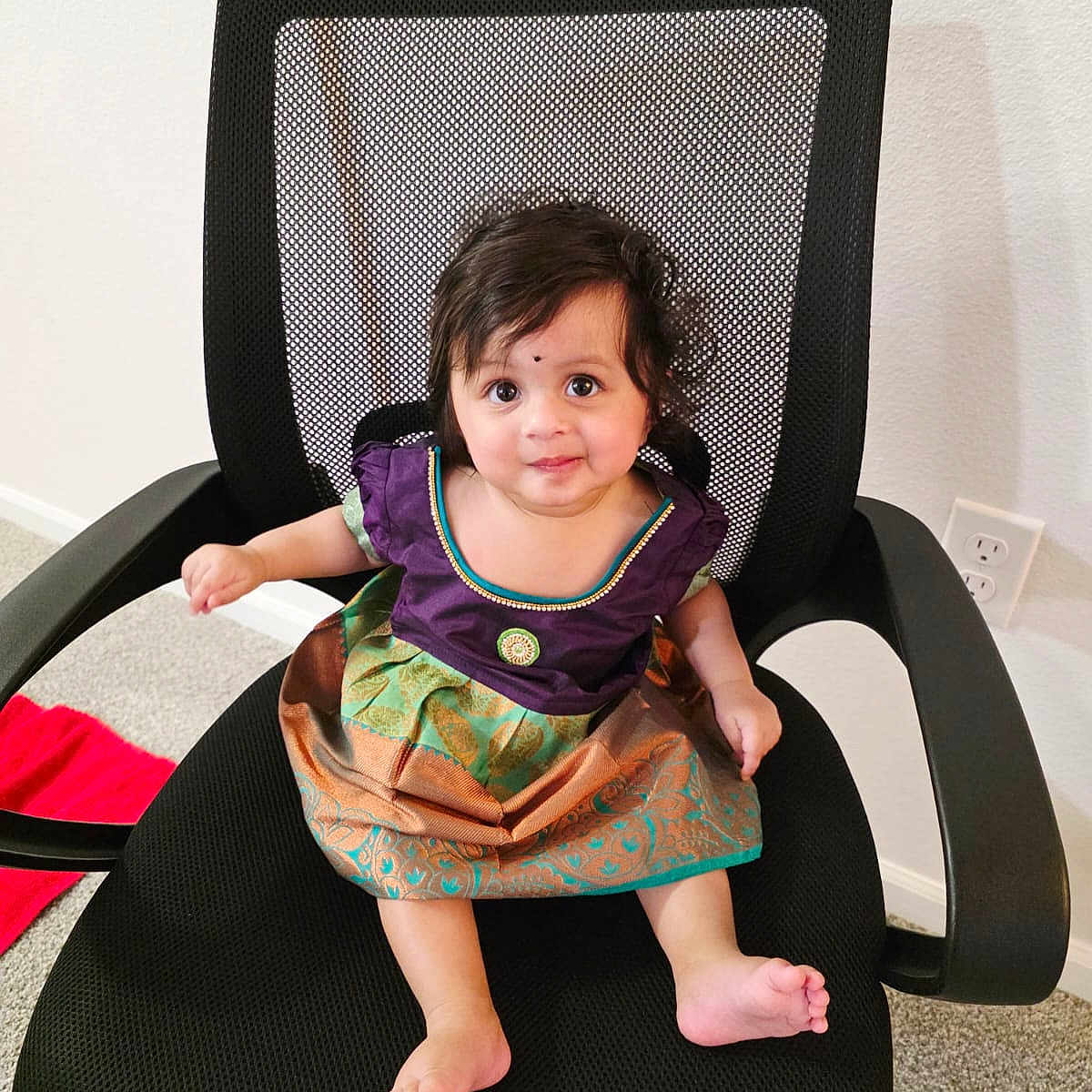 Shreekruti is registered to the contest to win money with this photo: baby, child, office_chair, mesh_chair, colorful_dress, traditional_clothing, barefoot, indoor, carpet, wall, power_outlet, cute, sitting, looking_up, black_chair, curly_hair, infant, young_child, adorable, portrait