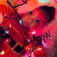 Ermias is registered to the contest to win money with this photo: baby, child, christmas_lights, red_clothing, santa_outfit, holiday, festive, cute, portrait, face, indoors, glowing, colorful, bright, cozy, winter, celebration, holiday_season, infant, warm