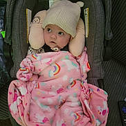 Cora is registered to the contest to win money with this photo: baby, bear_ears, blanket, car_seat, child, clothing, clouds, cozy, cute, indoor, infant, knit_hat, person, pink, plush_headrest, rainbow, resting, seatbelt, soft, wide_eyes