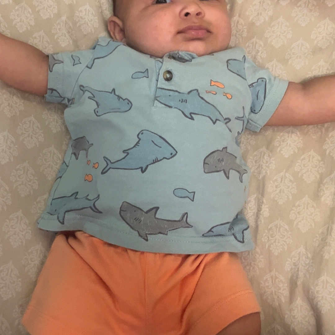 Elijah joined the competition — help win amazing prizes! arms_outstretched, baby, bed, casual, child, clothing, cute, feet, indoors, infant, lying_down, patterned_bedspread, person, portrait, shark_print, shirt, shorts, skin, socks, young_child