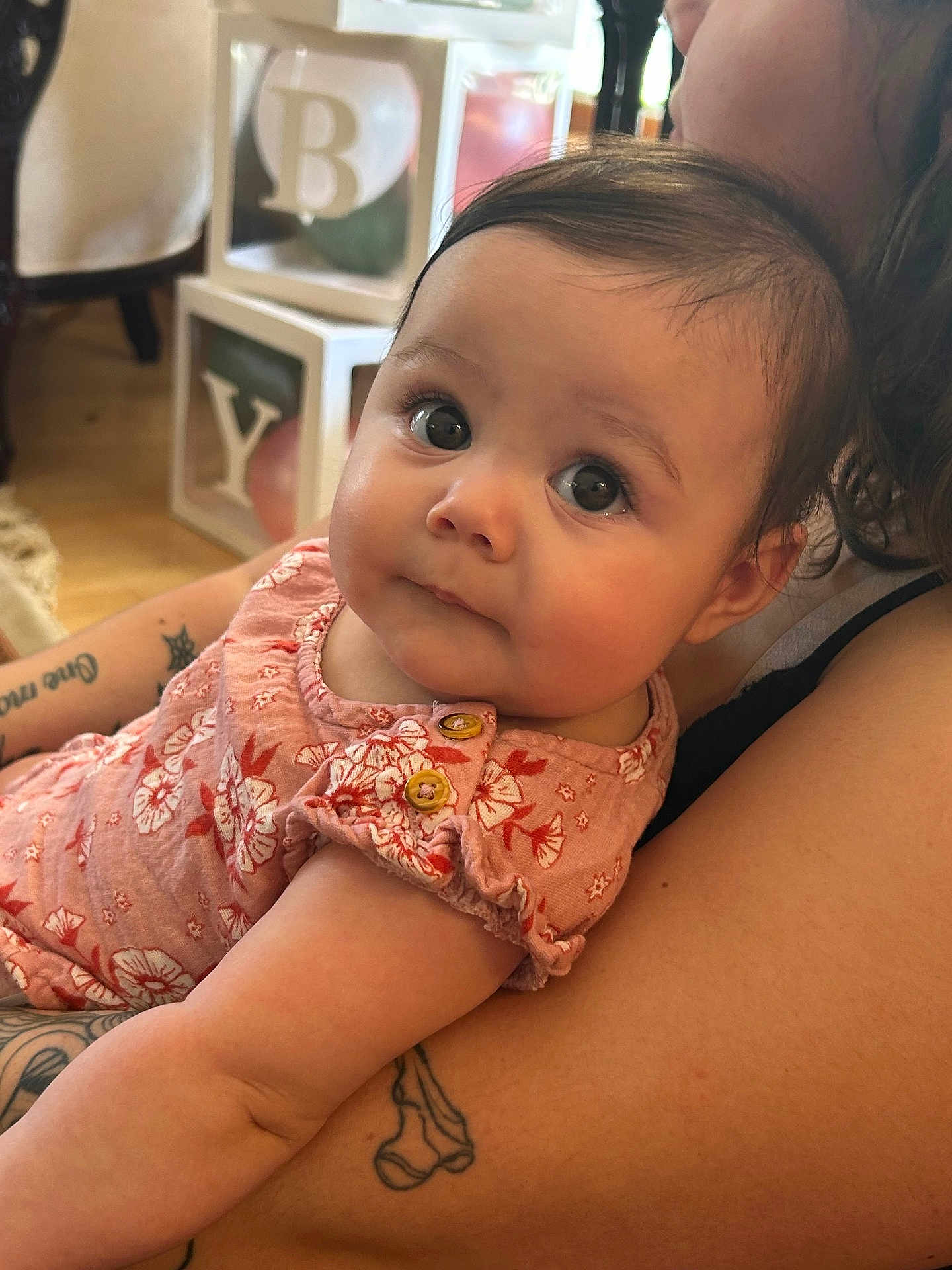 Jazlyn is registered to the contest to win money with this photo: baby, child, infant, person, arm, tattoo, clothing, pink, floral, face, eyes, indoor, furniture, blocks, decor, curious, skin, holding, portrait, closeup