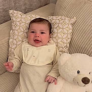 Kenzy a rejoint le concours — aidez-le/la à gagner de superbes lots ! baby, child, comfortable, couch, cozy, cream_outfit, cute, happy, holding, indoors, infant, patterned_pillow, pillow, plush_toy, seated, smiling, soft_texture, teddy_bear, toy, white