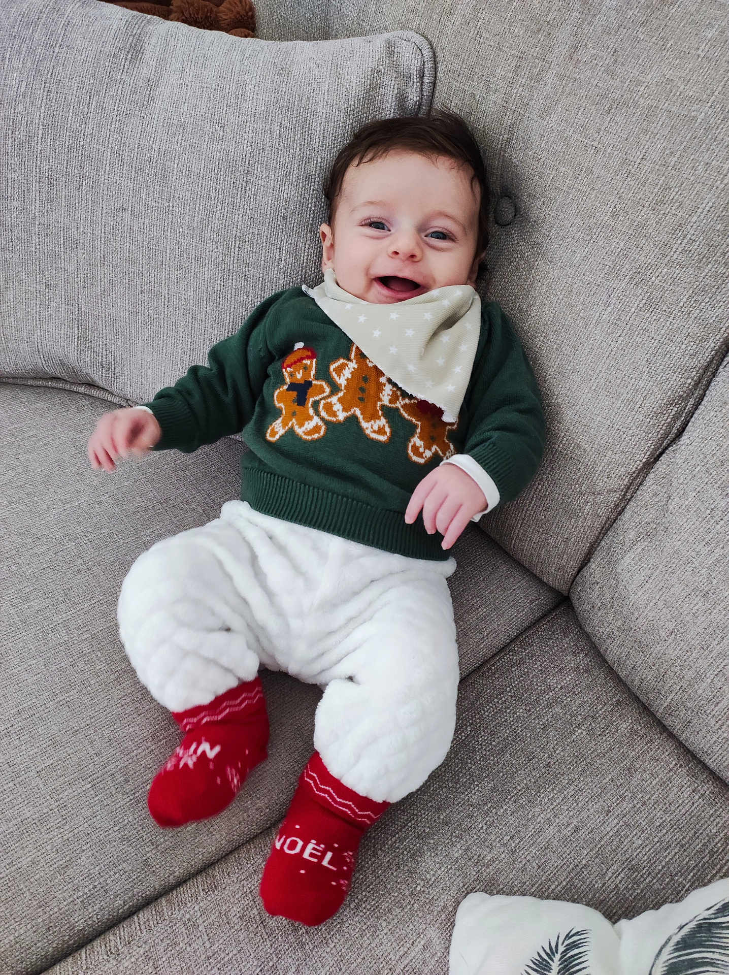 Clarence a rejoint le concours — aidez-le/la à gagner de superbes lots ! baby, smiling, couch, green_sweater, gingerbread_men, red_socks, white_pants, bandana, happy, infant, indoors, cozy, holiday, festive, cute, child, person, fabric, soft, relaxing