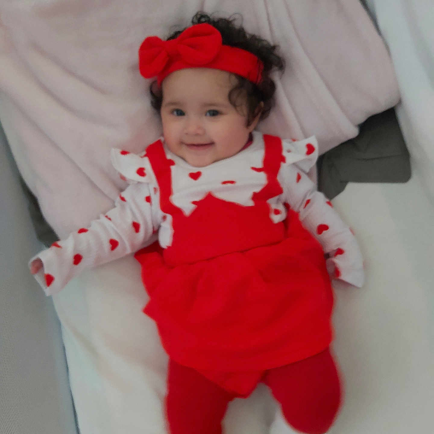 Thia a rejoint le concours — aidez-le/la à gagner de superbes lots ! baby, blanket, child, cozy, curly_hair, cute, happy, headband, heart_pattern, indoors, infant, lying_down, person, portrait, red_clothing, red_tights, resting, smile, soft_toys, white_socks