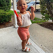 Camyla joined the competition — help win amazing prizes! toddler, child, popsicle, sidewalk, concrete, white_top, coral_shorts, white_sandals, bushes, car, suburban, outdoor, summer, playful, expression, person, standing, clothing, daytime, nature