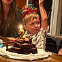 child, birthday, cake, brownie, candle, happy_birthday_headband, celebration, smiling_woman, table, indoor, party, excited, raising_hand, homemade_cake, food, family, portrait, childrens_party, lighting, fun