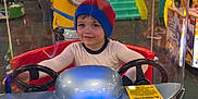 Oliver is registered to the contest to win money with this photo: child, beanie, arcade, kiddie_ride, minion, toy, indoor, play_area, steering_wheel, smiling, colorful, amusement, game, people, background, fun, metallic, seat, person, hat