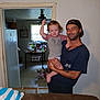 Jameson is registered to the contest to win money with this photo: child, toddler, man, indoor, living_room, kitchen, holding, cap, casual, smile, arm_raised, window, refrigerator, table, bottle, chair, doorway, furniture, person, home