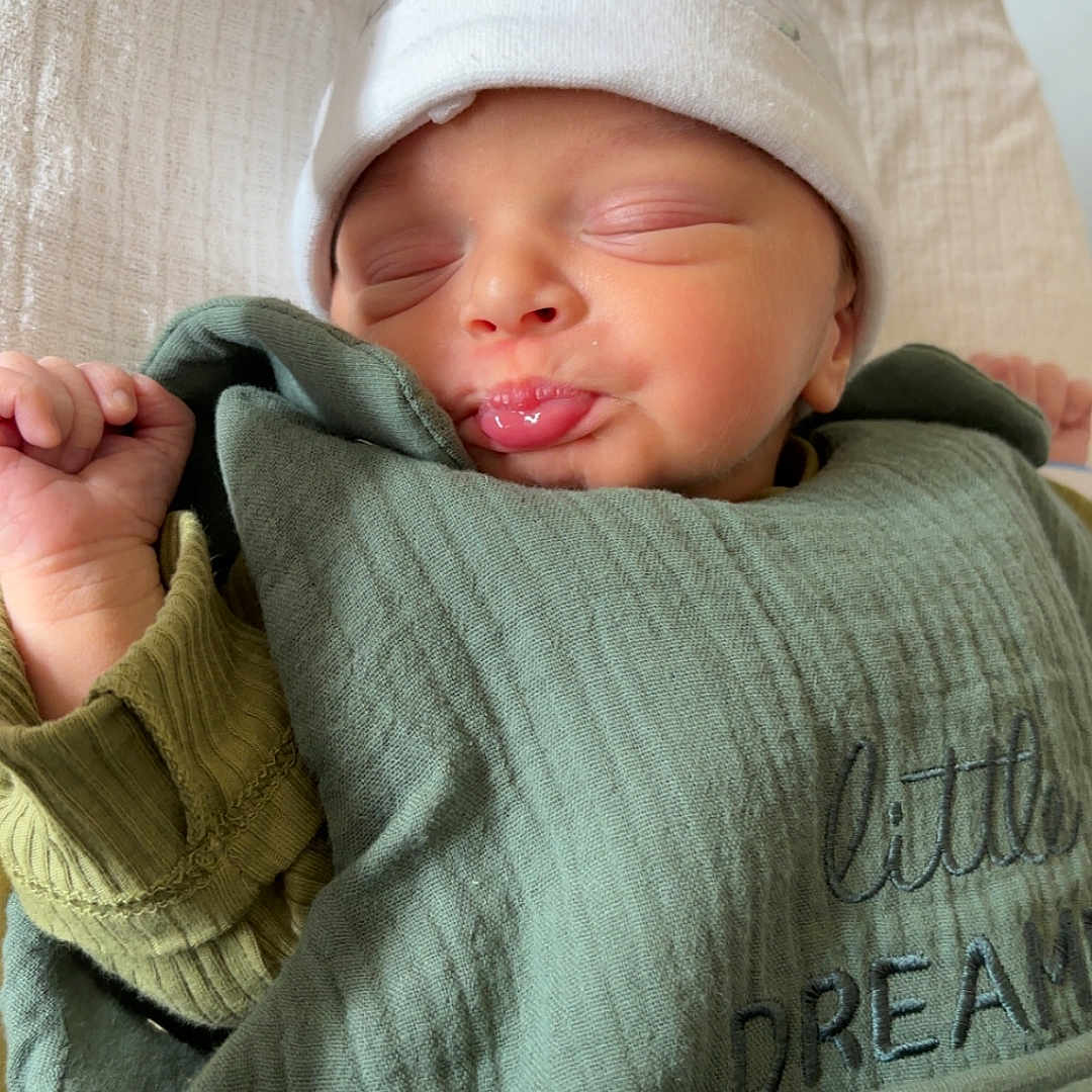April participe au concours pour gagner de l'argent avec cette photo : baby, newborn, sleeping, face, hat, blanket, green_blanket, pout, cute, infant, child, peaceful, soft, swaddled, clothing, hand, portrait, indoors, headwear, resting