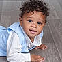 toddler, child, curly_hair, blue_vest, white_shirt, floor, wooden_floor, portrait, indoor, cute, smiling, hands, baby, crawling, person, young_child, looking_at_camera, curious, face, skin