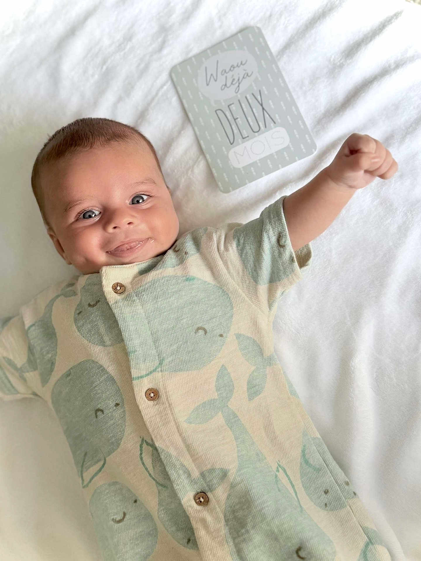 Ioni participe au concours pour gagner de l'argent avec cette photo : baby, infant, smiling, onesie, whale_pattern, blanket, milestone_card, happy, cute, lying_down, raised_arm, buttoned_clothing, cheeky, soft_texture, two_months, blue_eyes, short_hair, indoor, portrait, child