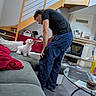 man, dog, puppy, couch, indoor, staircase, fireplace, glass_table, carpet, sitting, interaction, casual_clothing, living_room, modern_interior, pet, home, red_blanket, floor, furniture, relaxation