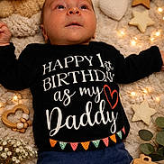 Vlad participe au concours pour gagner de l'argent avec cette photo : baby, infant, black_shirt, blue_pants, knitted_blanket, teddy_bear, heart_shape, star_shape, fairy_lights, wooden_toy, wooden_camera, flowers, greenery, lying_down, portrait, celebration, happy, cute, child, indoors