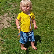Aries joined the competition — help win amazing prizes! toddler, child, grass, outdoor, sunlight, yellow_shirt, blue_shorts, barefoot, snack, shadow, summer, person, portrait, standing, greenery, daylight, casual_clothing, cute, young_child, playful