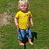 toddler, child, grass, outdoor, sunlight, yellow_shirt, blue_shorts, barefoot, snack, shadow, summer, person, portrait, standing, greenery, daylight, casual_clothing, cute, young_child, playful