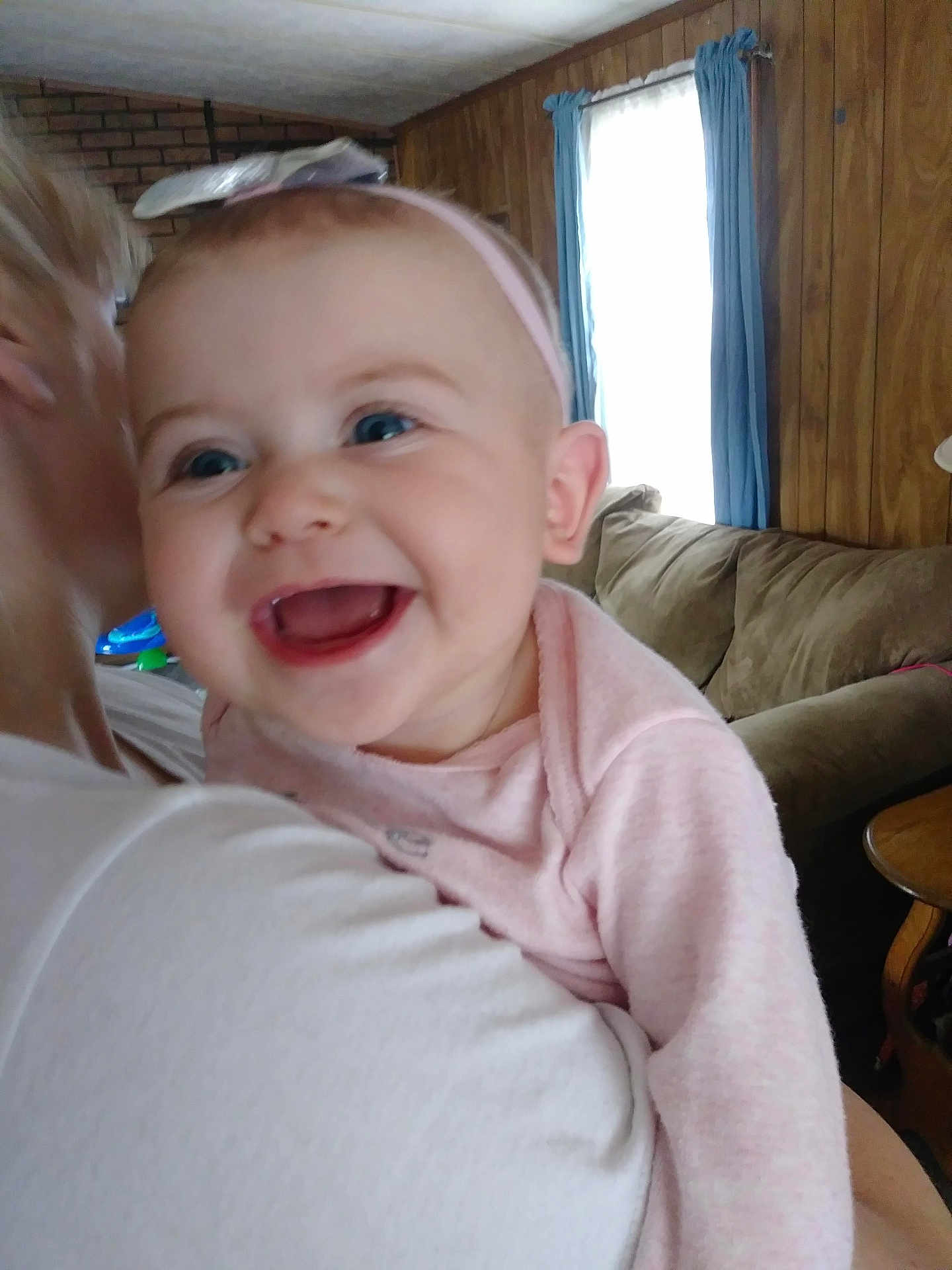 Ella joined the competition — help win amazing prizes! baby, smiling, headband, pink_clothing, infant, indoor, person, adult, couch, wood_paneling, window, curtains, holding, happy, closeup, face, child, casual, home, cheerful