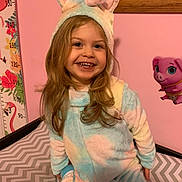 Ella joined the competition — help win amazing prizes! child, unicorn_onesie, smiling, indoor, pink_wall, height_chart, toy_pig, chevron_pattern, bed, furniture, happy, portrait, cute, costume, long_hair, young_child, face, clothing, room, playful