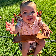 Millie joined the competition — help win amazing prizes! baby, child, high_chair, outdoor, grass, sunlight, happy, smiling, reaching, wood, clothing, person, cute, infant, summer, nature, portrait, baby_girl, bracelet, seat