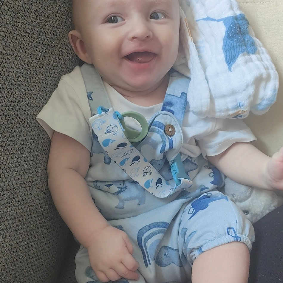 Kory is registered to the contest to win money with this photo: baby, blanket, blue, child, clothing, couch, cute, face, foot, hand, happy, indoors, infant, overalls, pale, person, sitting, skin, smiling, toy
