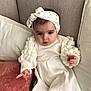 Emy a rejoint le concours — aidez-le/la à gagner de superbes lots ! baby, child, infant, dress, headband, bow, couch, pillow, white_clothing, cute, portrait, indoors, soft_texture, furniture, seated, person, young, expression, cozy, comfortable