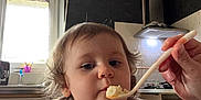 Athena a rejoint le concours — aidez-le/la à gagner de superbes lots ! toddler, child, feeding, spoon, high_chair, kitchen, appliance, window, curly_hair, bib, food, hand, person, indoor, chair, light, cooking, domestic, cute, meal