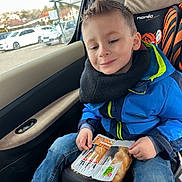 Lilio participe au concours pour gagner de l'argent avec cette photo : child, boy, car, car_seat, blue_jacket, jeans, snack, packaged_food, smile, seatbelt, window, daylight, casual, happy, portrait, indoor, seat, clothing, person, leisure
