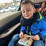 child, boy, car, car_seat, blue_jacket, jeans, snack, packaged_food, smile, seatbelt, window, daylight, casual, happy, portrait, indoor, seat, clothing, person, leisure