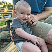 Liam joined the competition — help win amazing prizes! baby, smiling, infant, outdoor, bench, wood, person, adult, hand, clothing, shorts, tshirt, sunlight, nature, trees, park, skin, face, happy, portrait