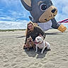 woman, dog, bulldog, beach, sand, inflatable, balloon, sky, cloud, smile, outdoor, pet, animal, happy, playful, casual_clothing, fun, daytime, recreation, nature