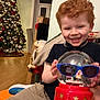 Oliver is registered to the contest to win money with this photo: child, boy, red_hair, smiling, snow_globe, sunglasses, christmas_tree, nutcracker, holiday_decor, indoor, happy, toys, festive, home, carpet, furniture, cheerful, portrait, seasonal, celebration