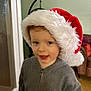 child, santa_hat, holiday, indoor, smile, face, hoodie, young_child, festive, red, white, gray, cute, portrait, person, cozy, warm_lighting, happy, home, christmas