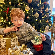 Oliver is registered to the contest to win money with this photo: child, red_hair, christmas_tree, gift_box, snow_globe, holiday, festive, decorations, indoor, floor, sweater, jeans, holiday_lighting, present, celebration, winter_clothing, home, relaxed, holiday_season, smiling