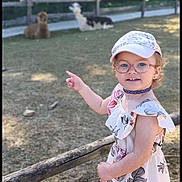 Mya participe au concours pour gagner de l'argent avec cette photo : alpaca, animal, cap, child, cute, daytime, dress, fence, girl, glasses, grass, happy, nature, outdoor, pointing, shoes, smiling, socks, sunlight, trees
