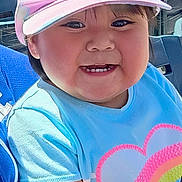 Cecilia is registered to the contest to win money with this photo: child, toddler, cap, pink_cap, blue_shirt, heart_design, smiling, happy, stadium, spectators, outdoor, sunlight, seated, person, casual_clothing, daylight, hat, cute, portrait, fun