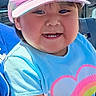 blue_shirt, cap, casual_clothing, child, cute, daylight, fun, happy, hat, heart_design, outdoor, person, pink_cap, portrait, seated, smiling, spectators, stadium, sunlight, toddler