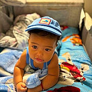 Jaci is registered to the contest to win money with this photo: baby, child, infant, blue_cap, bed, bedroom, blanket, bedspread, crawling, sitting, portrait, face, eyes, smiling, clothing, toy, stuffed_animal, indoor, home, colorful
